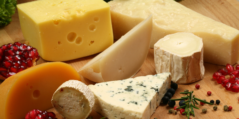 Assorted cheeses arranged on a wooden board with herbs and fruit