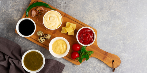 Wooden board with assorted condiments, cheese cubes, quail eggs, and herbs.