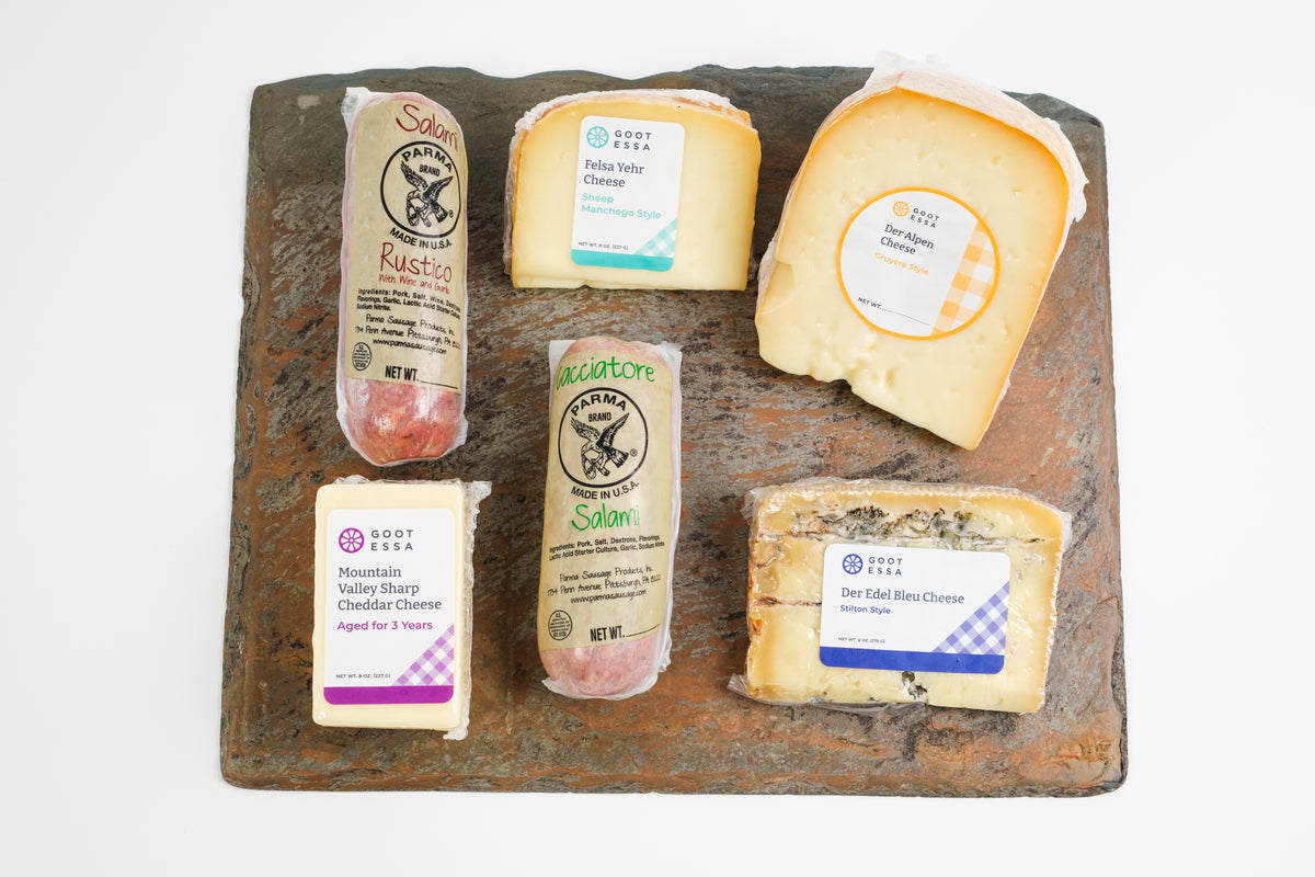 A selection of artisanal cheeses from Salom and Great Lakes Creamery arranged on a rustic, distressed wooden serving board against a clean white background.